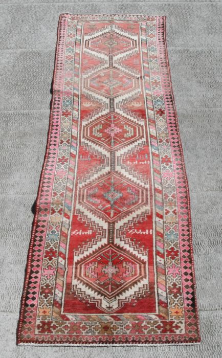 A Persian Azari runner with multiple hexagonal medallions on a beige ground, 350 by 90cms (374).