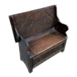 A carved oak monk's bench, the lift-up top carved with Heraldic style decoration, 106cms wide.