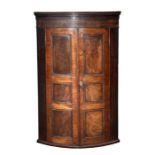 A George III bowfronted mahogany corner cupboard with twin panelled doors enclosing a shelved