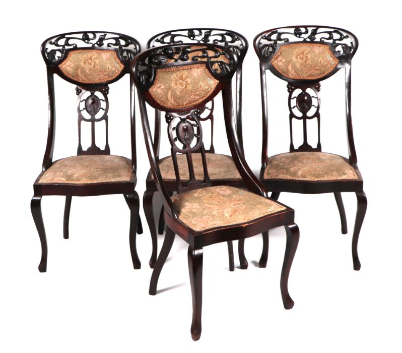 A set of four Art Nouveau mahogany dining chairs with carved and upholstered back rails, pierced