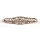 An Art Deco yellow metal bar brooch, the central square cut diamond set within a filigree mount,