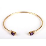 A gold (unmarked but tested for 9ct) bangle with amethyst set ends, 7cms diameter, 6.9g.