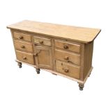 A pine dresser base, the central cupboard flanked by an arrangement of five drawers, on turned feet,