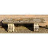 A large and very heavy well weathered reconstituted stone bench on scroll supports, 168cms.