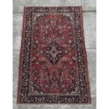 A Persian rug with central blue medallion on a red ground with floral motifs within a floral multi