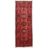 A Persian woollen runner with three central guls within borders, on a red ground, 300 by 100cms (