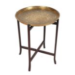 An Indo-Persian brass tray-top table on a folding hardwood base, 43cms diameter.