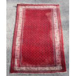 A Persian hand knotted rug with repeated geometric design within a multi border, on a red ground,