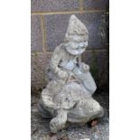 A reconstituted stone garden statue depicting a gnome riding a tortoise, 51cms high.
