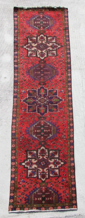 A Persian hand knotted runner with repeat star design within floral borders, on a red ground, 380 by