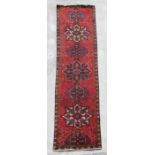 A Persian hand knotted runner with repeat star design within floral borders, on a red ground, 380 by