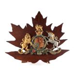 A polychrome cast iron heraldic plaque mounted on a Maple leaf shaped wooden back board. Overall
