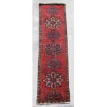 A Persian hand knotted runner with repeat star design within floral borders, on a red ground, 380 by