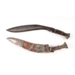 A horn handled kukri in a wooden scabbard with white metal overlay decoration depicting an