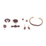 A selection of garnet set jewellery to include a bangle; a flowerhead cluster brooch; a half moon