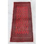 A Persian Turkoman woollen hand-made small rug with geometric designs on a red ground, 130 by