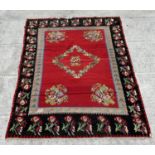 A large Romanian kilim rug with floral motifs on a red ground within a repeating floral border,