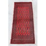 A Persian Turkoman woollen hand-made small rug with geometric designs on a red ground, 130 by