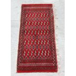 A Persian Turkoman woollen hand-made small rug with geometric designs on a red ground, 126 by
