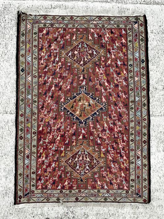 A Persian flatweave rug decorated with a multitude of stylised animals within a geometric border, on