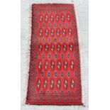 A Persian Turkoman woollen hand-made small rug with geometric designs on a red ground, 130 by