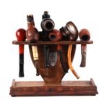 A six division oak pipe rack with a selection of pipes to include a Black Forest style white metal