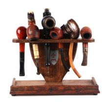 A six division oak pipe rack with a selection of pipes to include a Black Forest style white metal