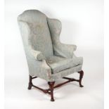 A Georgian upholstered high backed winged armchair with walnut carved dwarf cabriole front legs