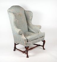 A Georgian upholstered high backed winged armchair with walnut carved dwarf cabriole front legs