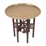A Middle Eastern brass tray table decorated with Egyptian figures, 64cms diameter, on a folding