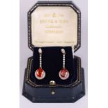 A pair of 9ct gold drop earrings set with a central burnt orange stone and diamonds.