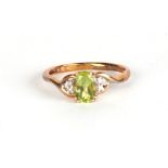 A 9ct gold dress ring set with an oval pale green stone (possibly peridot) and diamond shoulders,