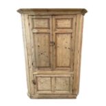 A large stripped pine free standing corner cupboard, the pair of panelled doors enclosing a