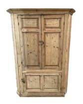 A large stripped pine free standing corner cupboard, the pair of panelled doors enclosing a