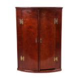 A 19th century figured mahogany bowfronted hanging corner cupboard, the pair of panelled doors