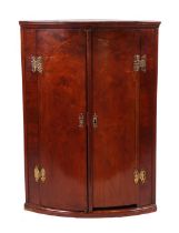 A 19th century figured mahogany bowfronted hanging corner cupboard, the pair of panelled doors