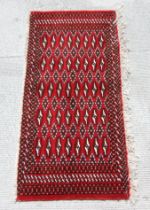 A Persian Turkoman woollen hand-made small rug with geometric designs on a red ground, 126 by