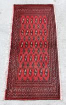 A Persian Turkoman woollen hand-made small rug with geometric designs on a red ground, 130 by