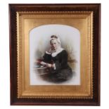 A Victorian tinted photograph depicting an old lady seated at a desk, 24 by 28cms, in a gilt box
