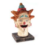 A contemporary mixed media painted clowns head mounted on a wooden plinth, 40cms high.
