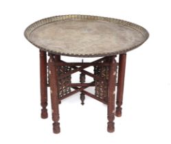 A large Middle Eastern brass tray-top table on a folding wooden stand, 73cms diameter.