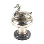 An accessory car mascot in the form of a swan, mounted on a plinth.