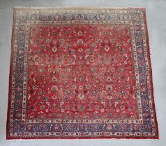 A large Persian hand knotted woollen rug decorated with foliate scrolls, on a red ground, 310 by