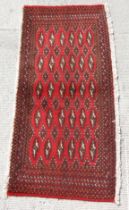 A small Persian Turkoman woollen hand-made rug with geometric designs on a red ground, approx 130 by