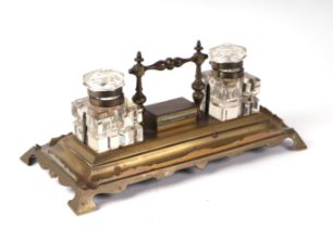 An Edwardian brass desk stand with central stamp box and two cut glass inkwells, 33cms wide.