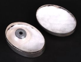 A prosthetic glass eye in a continental silver metal case engraved 'RG'.