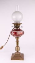 A Victorian oil lamp with brass stepped base, turned column, cranberry lustre glass reservoir and