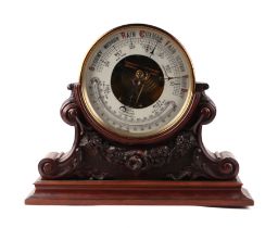 An Edwardian aneroid barometer in a gilt metal case, 20cms diameter, mounted in a carved mahogany