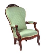 A Victorian mahogany upholstered armchair with carved back rail, scroll arms and turned front legs.