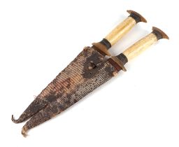 A pair of African tribal daggers, having matching bone and horn hilts, twin double edged blades, and
